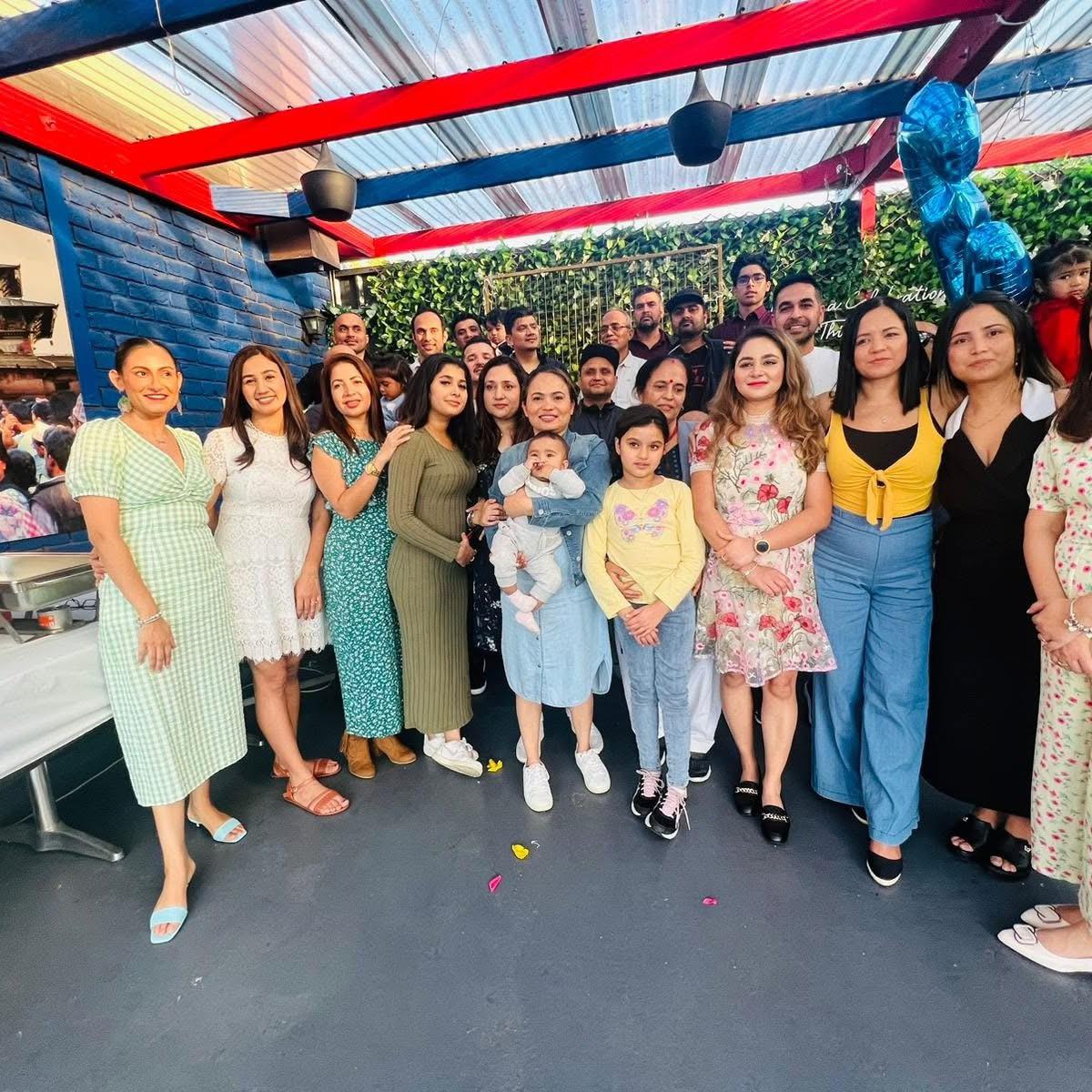 A large group of people gathered at a function, including adults of different ages, a woman holding a baby, and a few children. They are posing for a group photo, all smiling and enjoying themselves. Attire ranges from casual to semi-formal at Third Eye Windsor, 515 George St, South Windsor NSW 2756.