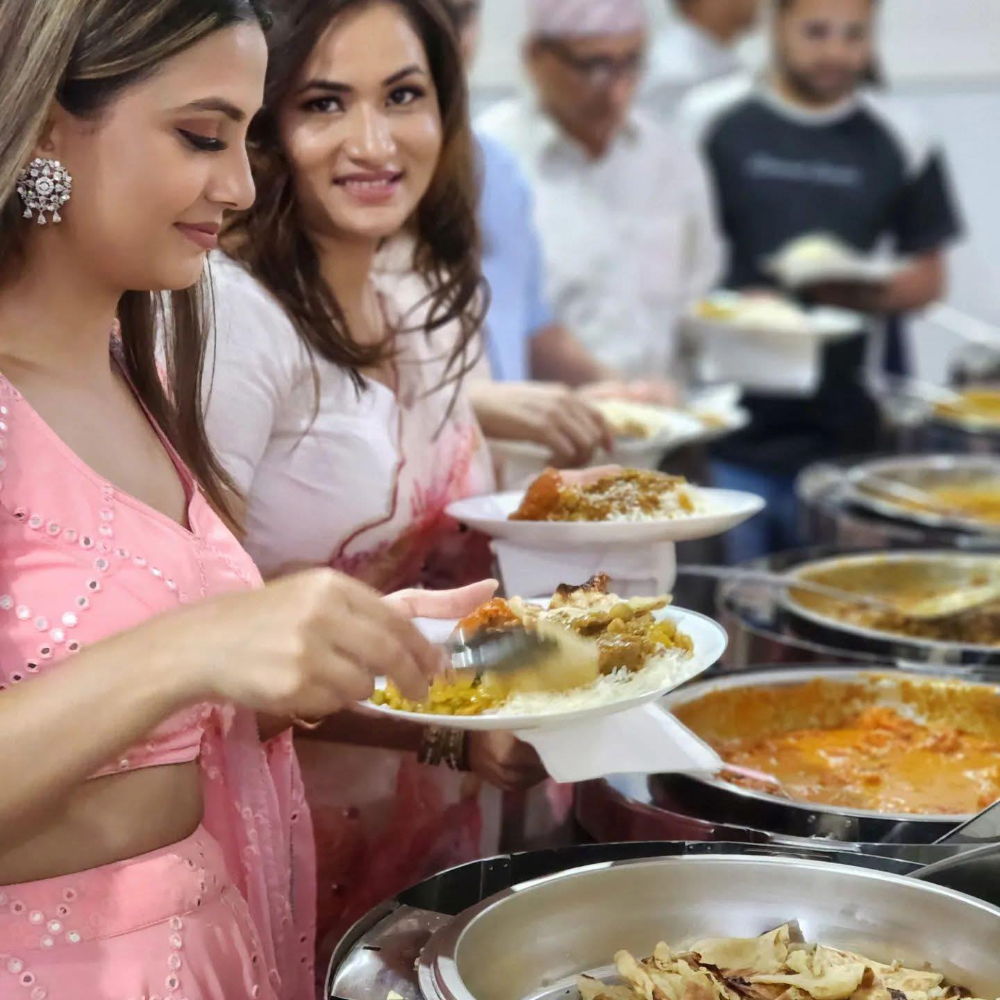 Two women smiling and serving themselves food from a buffet line. They are holding white plates with Indian and Nepalese cuisine at Third Eye Windsor, 515 George St, South Windsor NSW 2756.